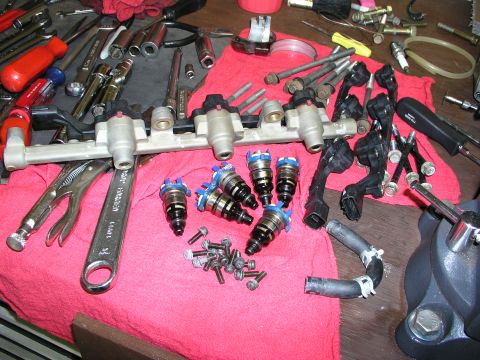 1996 Ford Probe - Disassembled fuel injectors and fuel rail with assorted tools and hardware on a workbench.