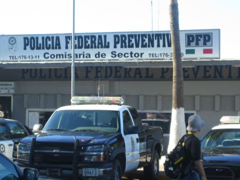 1990 Ford Bronco - black and white police pickup truck parked outside a Mexican 'Policia Federal Preventiva' (PFP) building, with a person standing in the for…