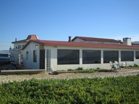 1990 Ford Bronco - single-story white building with a tile roof and large windows, with patio chairs and ground-cover plants in front under a clear sky.