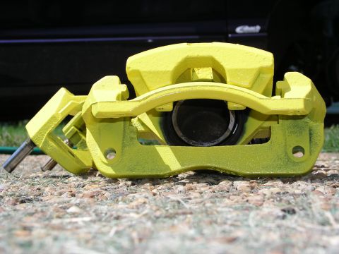 1996 Ford Probe - A bright yellow brake caliper sits on gravel, with a dark vehicle in the background.