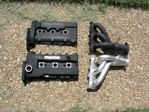 1996 Ford Probe - Engine parts, including valve covers and exhaust manifolds, are displayed on a gravel surface.