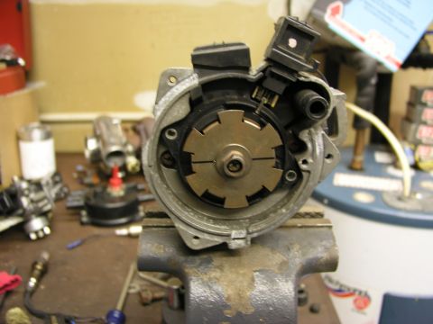 1996 Ford Probe - A disassembled distributor is held in a vise on a workbench, surrounded by other engine parts.