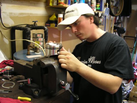 1996 Ford Probe - A person is working on a car engine piston, which is secured in a vise in a garage setting.