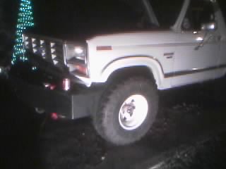 1986 Ford Bronco - A white Ford truck is shown from the front quarter panel with a large tire and aftermarket bumper.