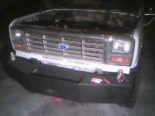 1986 Ford Bronco - Front view of a 1986 Ford Bronco, showing its grille and an aftermarket bumper. The hood is open, revealing the engine bay.