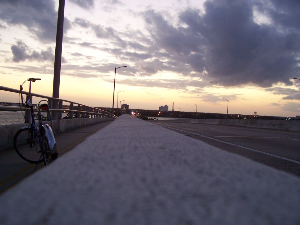 Bicycle parked on a bridge railing with a sunset sky and city skyline in the distance