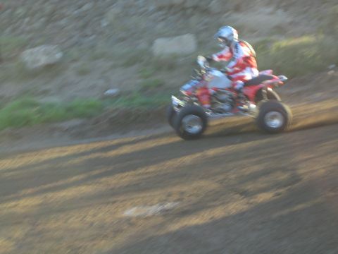 1990 Ford Bronco - rider in red leathers pilots a red-and-white racing quad along a dirt track beside a rocky embankment.