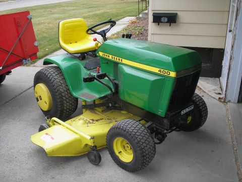 1990 Ford Bronco - A green and yellow John Deere 400 lawn tractor is parked on a concrete driveway next to a house.
