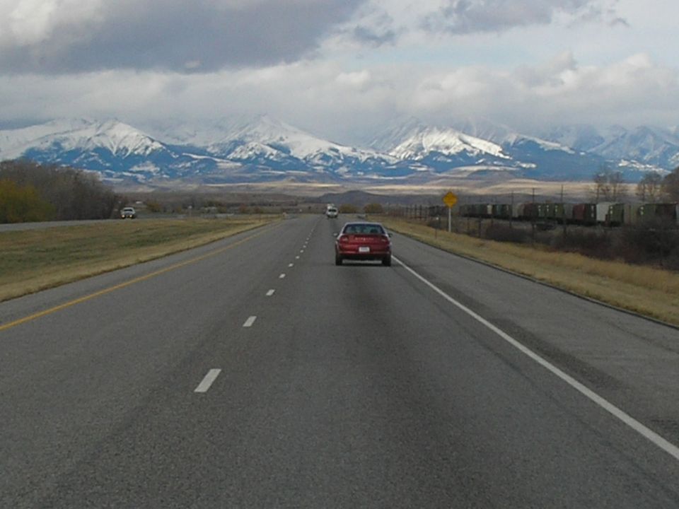 Red sedan driving on a highway with snow-capped mountains in the background