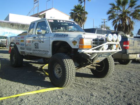 1990 Ford Bronco - white off-road race truck numbered 1600, with a roof light bar and tube front bumper, sits parked among other vehicles.
