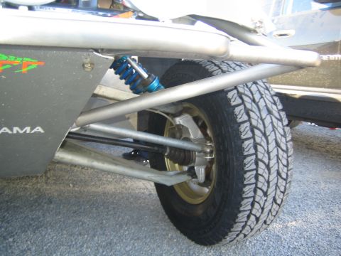 1990 Ford Bronco - Close-up of a race truck's rear suspension showing a blue coilover shock, tube control arms and an all-terrain tire.