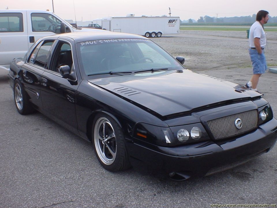 Black Mercury Marauder sedan with mesh grille and bra parked at a track with trailers behind