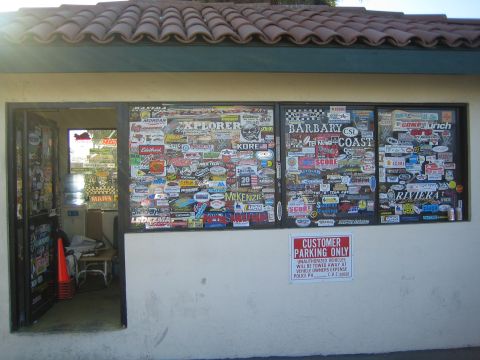 1990 Ford Bronco - windows of a tile-roofed stucco building are densely plastered with racing and brand stickers beside a parking-only sign.