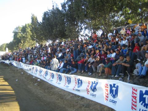 1990 Ford Bronco - large crowd of spectators sits on a tree-lined dirt hillside behind a white Tecate Light barrier banner.
