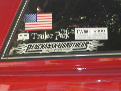 1990 Ford Bronco - Close-up of a red vehicle's rear quarter window with decals including a US flag, 'Trailer Park', 'TWW #100' and 'Penchansky Brothers'.