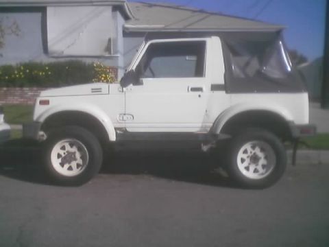 1990 Ford Bronco - white lifted soft-top Suzuki Samurai sits on a residential driveway with the convertible top up.