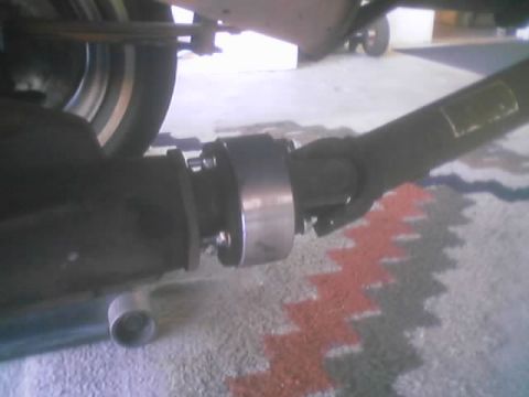 1990 Ford Bronco - close-up of a driveshaft slip yoke and U-joint beneath a vehicle parked over a rug.