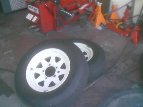 1990 Ford Bronco - Two white eight-spoke steel wheels with tires lie on a garage floor near jack stands and a tire machine.