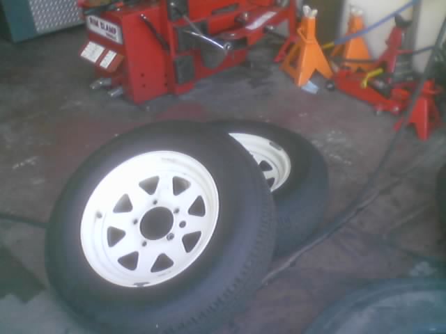 Two white-spoke wheels with tires in a garage with jack stands