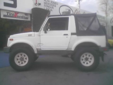 1990 Ford Bronco - white lifted soft-top Suzuki Samurai with door open sits in front of a TireXperts shop sign.