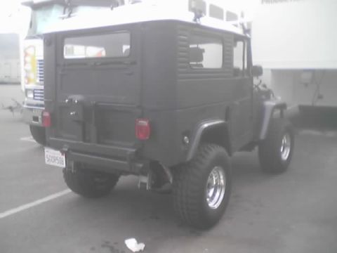 1990 Ford Bronco - gray lifted FJ40-style hardtop 4x4 with white roof and chrome wheels parked beside a truck and trailer.