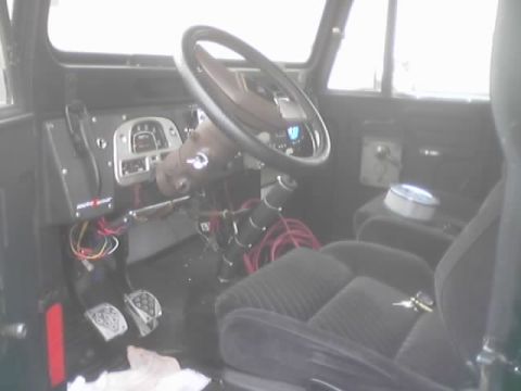 1990 Ford Bronco - Interior of a vintage 4x4 showing the steering wheel, exposed gauges, shifter and cloth bucket seat.