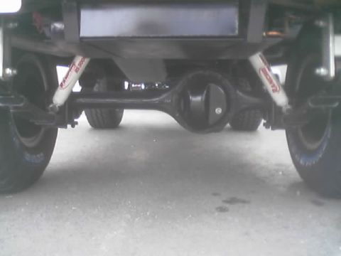 1990 Ford Bronco - Rear underbody view showing a solid axle, red Rancho shocks and tires of a lifted vehicle.