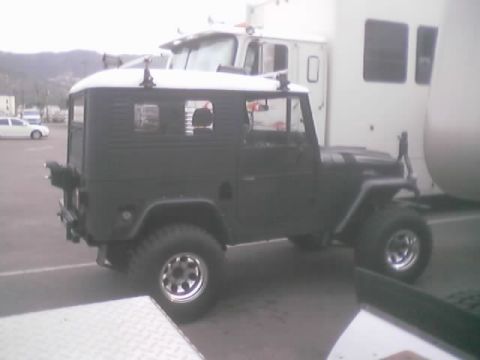 1990 Ford Bronco - gray lifted hardtop 4x4 with white roof parked near a service truck in an asphalt lot.
