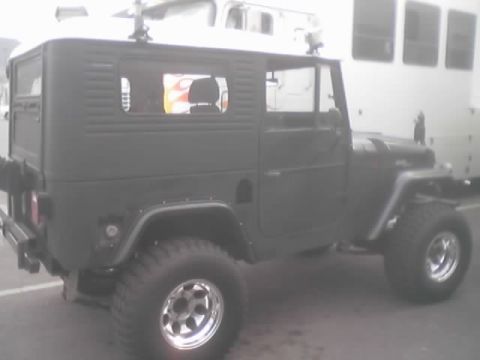 1990 Ford Bronco - Side profile of a gray lifted hardtop 4x4 with chrome wheels, a flamed truck reflected in its window.