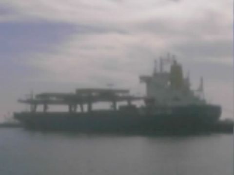 1990 Ford Bronco - dark cargo ship sits on calm water beneath an overcast sky in a hazy distant view.