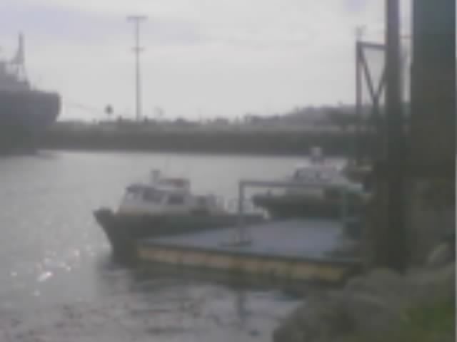 Small boats moored at a dock with a larger ship behind