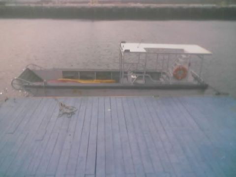 1990 Ford Bronco - gray open launch boat with a white canopy and orange life ring sits moored beside a weathered dock.