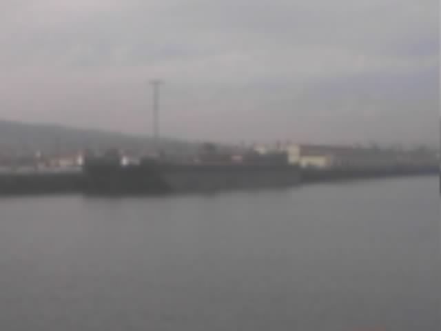 Blurry overcast view of a dark cargo ship docked at an industrial waterfront