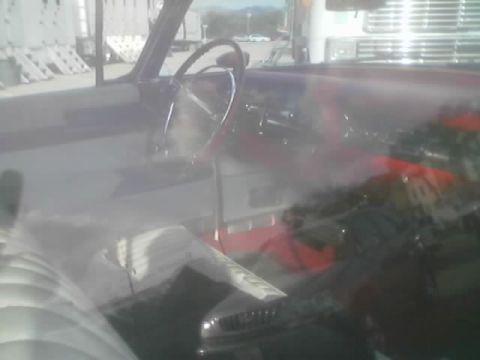 1990 Ford Bronco - Looking through a sun-glared windshield into a vintage car's interior with steering wheel and red upholstery.