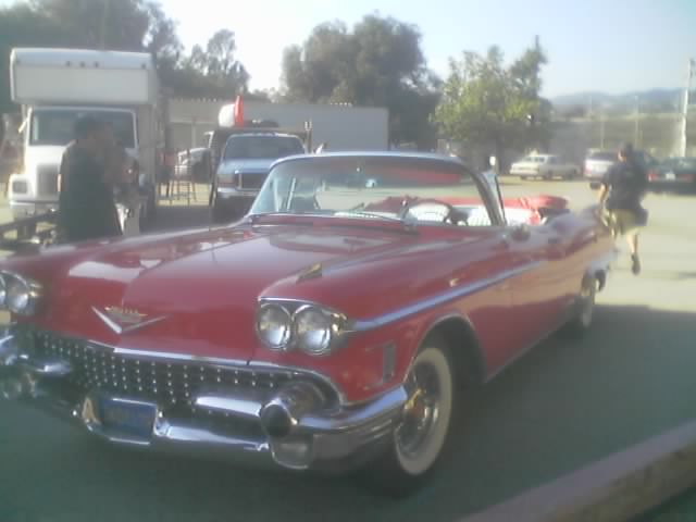 Red 1958 Cadillac convertible parked near box trucks and pickups