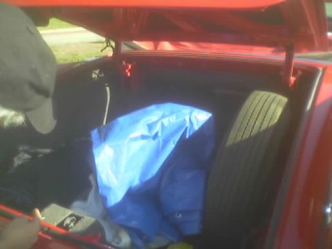 1990 Ford Bronco - open trunk of a red car reveals a blue tarp bundle alongside a spare tire, a person leaning in at left.