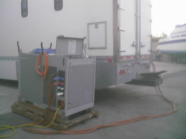 Gray generator unit on wooden pallet connected to trailer with orange and yellow cables