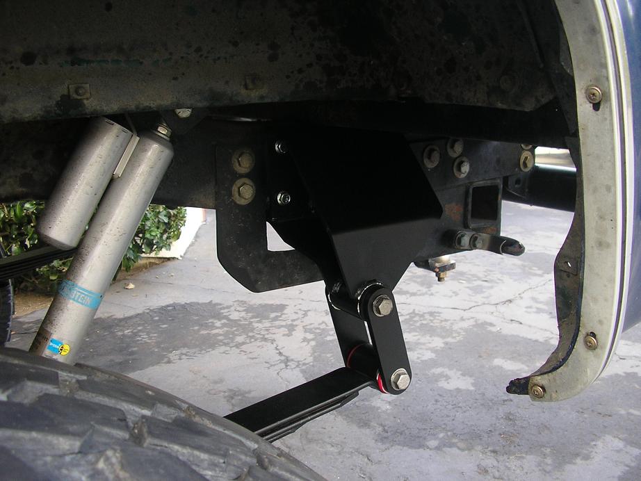 Underbody view of black welded shackle bracket and shock mount with reservoir shock above tire