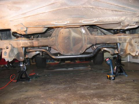 1985 Ford LTD Crown Victoria - The rear suspension and differential of a vehicle are visible, supported by jack stands.
