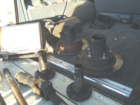 1988 Ford Bronco - Various vehicle axle components, such as hubs, brake rotors, and driveshaft parts, are organized inside a vehicle's cargo area.