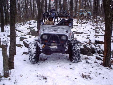 1989 Ford F-350 - An off-road vehicle navigates a snowy, wooded terrain with another vehicle visible in the background.