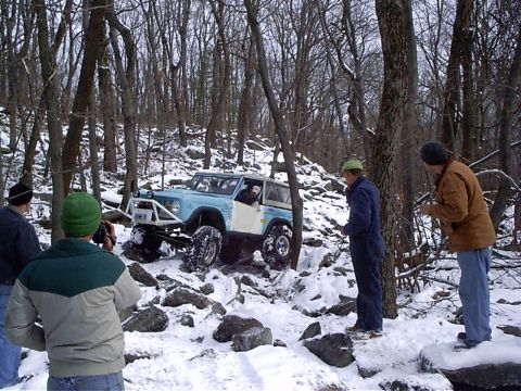 1989 Ford F-350 - A modified light blue off-road vehicle tackles a snowy, rocky trail with onlookers observing.