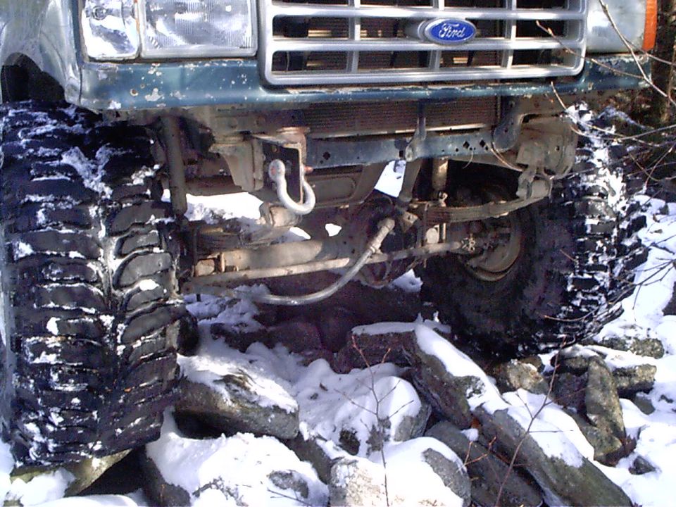 1989 Ford F-350 front end with large off-road tires on rocky, snowy terrain