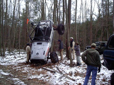 1989 Ford F-350 - An off-road vehicle is overturned in a snowy wooded area with several people observing.