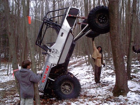 1989 Ford F-350 - An off-road vehicle is stuck between two trees in a snowy wooded area, with onlookers observing the situation.