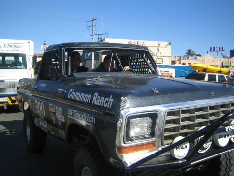 1990 Ford Bronco - gray late-1970s Ford pickup race truck marked '300', 'Cinnamon Ranch' and 'BFGoodrich' in a Mexican street.