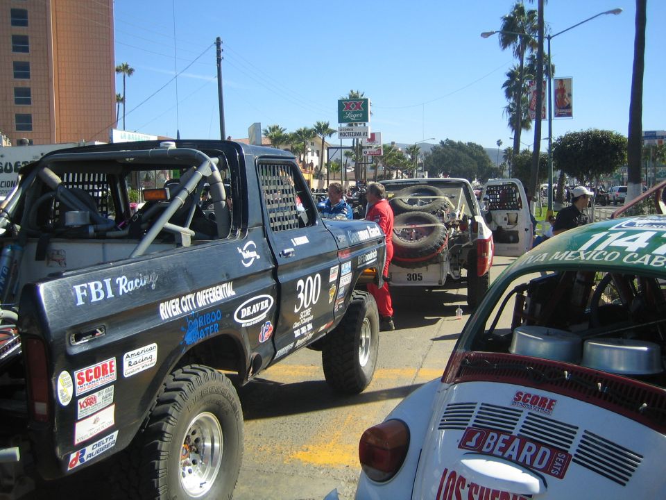 Off-road race vehicles staged on a street, a Ford truck and a Baja Bug