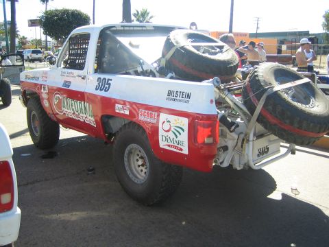1990 Ford Bronco - red and white #305 off-road race truck lettered California Tomatoes, carrying lashed-down spare tires at the rear.