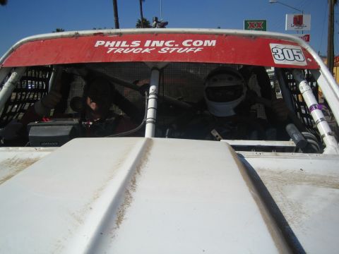 1990 Ford Bronco - View through the windshield of #305 showing a helmeted driver and passenger inside, with red header lettered Phils Inc.com Truck Stuff.