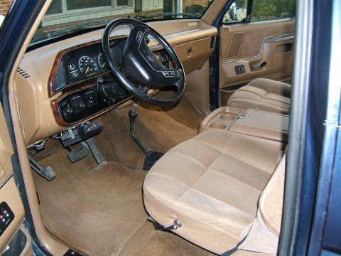 1988 Ford Bronco - The interior of a 1987 Ford Bronco shows tan cloth seats and a dashboard with wood grain trim.